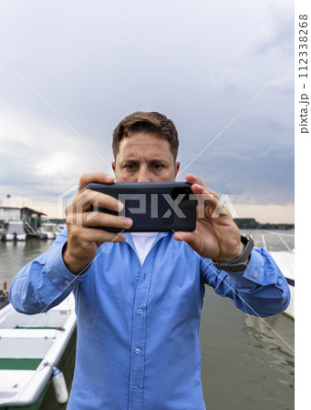 Man holding smartphone in his hands at river and taking photographs 112338268