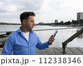 Man holding smartphone in his hand beside the river at port. Nautical and marine concept 112338346