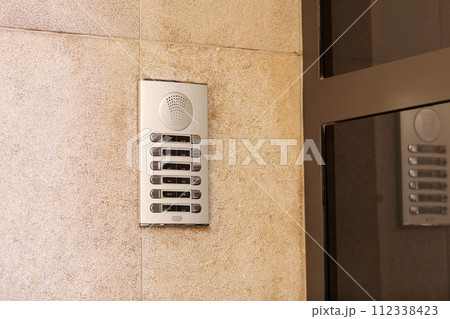 Outdoor intercom outside a residential building with empty name tag cards. Silver modern doorbells with blank nameplates suitable for adding text. European intercom communication system 112338423
