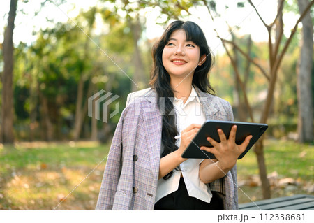 Shot of confident businesswoman holding digital tablet and looking away sitting in park Shot of confident businesswoman holding digital tablet and looking away sitting in park 112338681