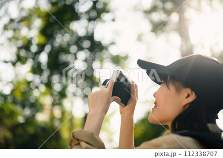 Happy young woman trekking among trees and taking pictures with vintage camera Happy young woman trekking among trees and taking pictures with vintage camera 112338707