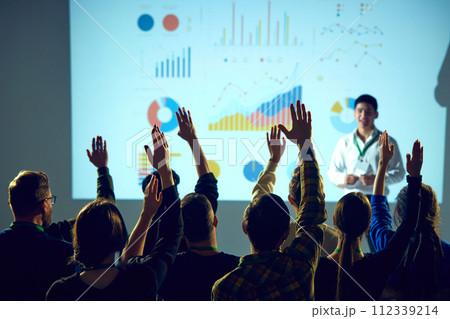 Interactive business workshop with participants engaging with presenter, business coach in front of graphical data analysis. Interactive business workshop with participants engaging with presenter, business coach in front of graphical data analysis. 112339214
