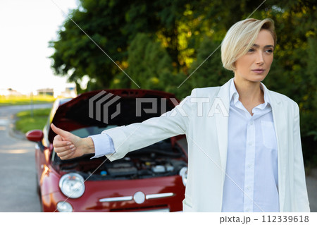 Businesswoman raises her finger while standing on country road needs help with her broken car Businesswoman raises her finger while standing on country road needs help with her broken car 112339618