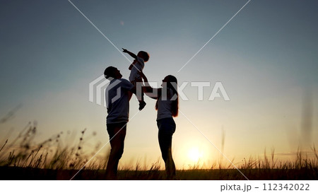 family standing on the field. happy childhood concept for little child. big happy family stands on field, parents raised the lifestyle child in their arms, sunset on the background, silhouettes 112342022