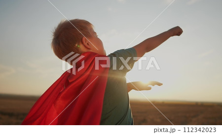 boy with the cloak. concept of a happy childhood and family for a child. a child in a superhero costume stretched his hand forward, a red cape and a blue T-shirt, sunset on the background lifestyle boy with the cloak. concept of a happy childhood and family for a child. a child in a superhero costume stretched his hand forward, a red cape and a blue T-shirt, sunset on the background lifestyle 112342023