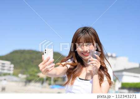 飲み物片手にスマホで撮影する女性 112343271