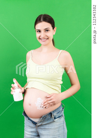pregnant woman in opened jeans applying cream against stretch marks on her belly at colorful background with copy space. Skin care during pregnancy concept pregnant woman in opened jeans applying cream against stretch marks on her belly at colorful background with copy space. Skin care during pregnancy concept 112343382