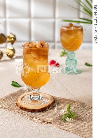 Cold longan juice with ice in a glass, on the dining table decorated by the window with evening light. 112344698