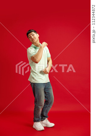 Happy, joyful man, student in denim jeans and T-shirt dancing in motion against red studio background. Success. Happy, joyful man, student in denim jeans and T-shirt dancing in motion against red studio background. Success. 112344872
