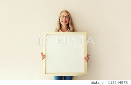 Woman decorating interior, hanging white blank photo frame, wooden picture on wall in new house 112344978