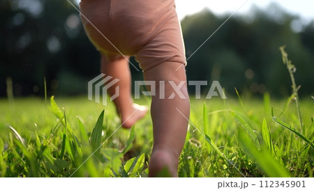 baby takes first steps in the park. happy family kid dream concept. dad teaches his son to walk takes the first steps in the park on green grass. baby son taking first lifestyle steps 112345901