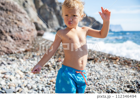 Beautiful blond child 2.5 years old in swimming trunks at the sea on a sunny warm summer day Beautiful blond child 2.5 years old in swimming trunks at the sea on a sunny warm summer day 112346494