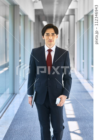 オフィスの廊下を歩くスマホを持ったスーツ姿のビジネスマン 112346943