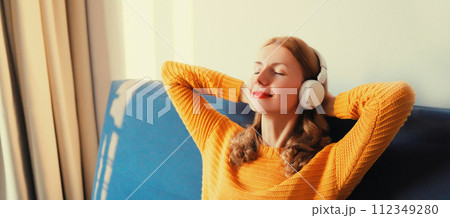 Happy relaxed young woman listening to music with headphones lies on couch at home 112349280