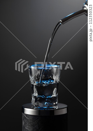 Vodka pouring from the bottle into a glass on a dark background. Vodka pouring from the bottle into a glass on a dark background. 112350323