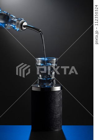 Vodka pouring from the bottle into a glass on a dark background. 112350324