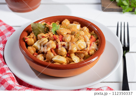 Close up. Ropa vieja, typical Canarian dish of chickpeas stew on earthenware casserole on white table. Close up. Ropa vieja, typical Canarian dish of chickpeas stew on earthenware casserole on white table. 112350337
