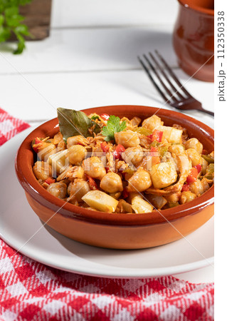 Homemade Ropa vieja, typical Canarian dish of chickpeas stew in earthenware casserole on white table. Vertical format. Homemade Ropa vieja, typical Canarian dish of chickpeas stew in earthenware casserole on white table. Vertical format. 112350338