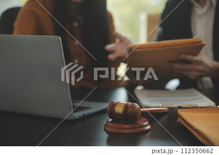 Justice and Law concept. Legal counsel presents to the client a signed contract with gavel and legal law or legal having team meeting at law firm in background 112350662