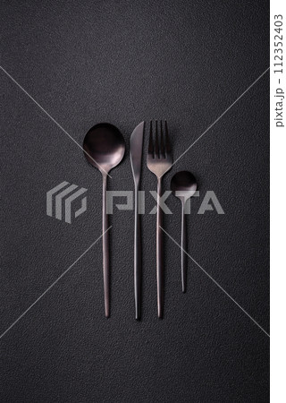 Cutlery fork, knife and spoon on a dark textured concrete background 112352403