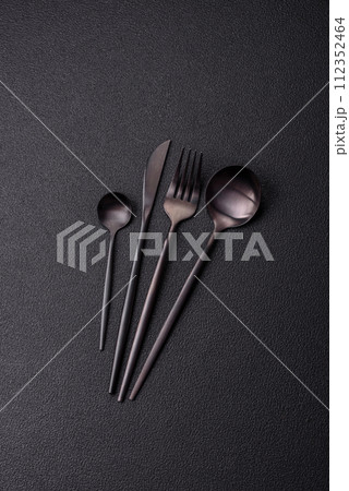 Cutlery fork, knife and spoon on a dark textured concrete background Cutlery fork, knife and spoon on a dark textured concrete background 112352464