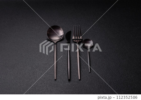 Cutlery fork, knife and spoon on a dark textured concrete background Cutlery fork, knife and spoon on a dark textured concrete background 112352586