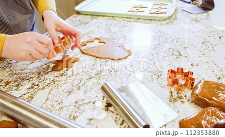 Using various festive cookie cutters, we're cutting out charming gingerbread cookies from the rolled dough on the sleek marble counter, bringing holiday cheer to the modern kitchen. 112353880