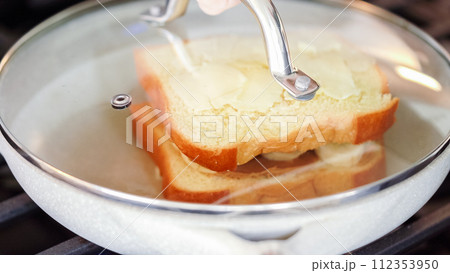 Within the sleek setting of a modern white kitchen, banana slices and brioche bread sizzle on a non-stick pan over a gas stove, setting the stage for an enticing grilled peanut butter banana sandwich. Within the sleek setting of a modern white kitchen, banana slices and brioche bread sizzle on a non-stick pan over a gas stove, setting the stage for an enticing grilled peanut butter banana sandwich. 112353950