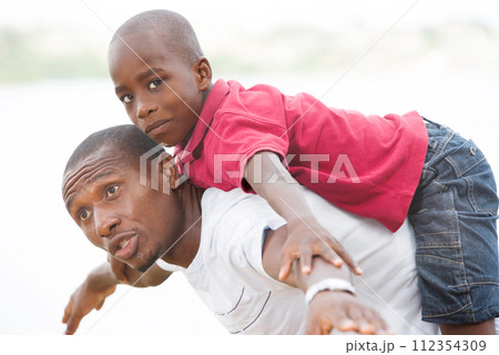 young father carrying his son smiling on his back young father carrying his son smiling on his back 112354309