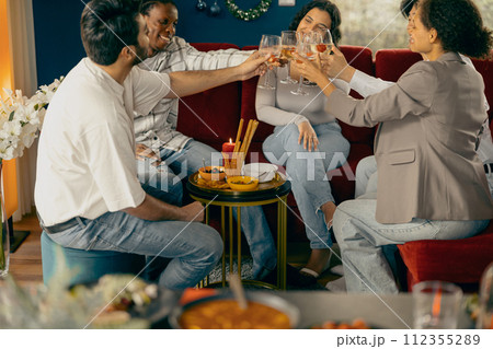 Group of happy friends is drinking cocktails and clinking glasses having holiday dinner party 112355289