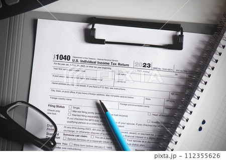 A tax form is on a clipboard with a pen next to it A tax form is on a clipboard with a pen next to it 112355626