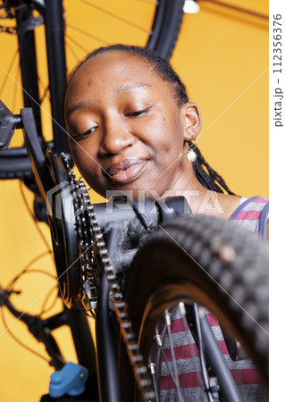 Detailed view of black woman carefully examining bicycle chain stay for optimal cycling. Young lady in up-close shot, showcases her attention to detail as she diligently maintains her bike components. Detailed view of black woman carefully examining bicycle chain stay for optimal cycling. Young lady in up-close shot, showcases her attention to detail as she diligently maintains her bike components. 112356376