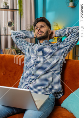 Young man freelancer sitting on couch close laptop pc after finishing work in living room at home 112356905
