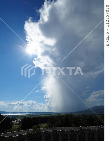 真夏の午後、湧き上がる積乱雲と雨柱と白く輝く太陽が青空に印象的で綺麗だ。 112357030