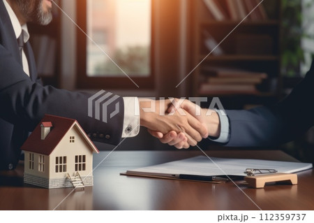 Real estate agent shaking hands with customer with miniature simple house on a table 112359737