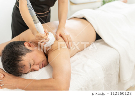 メンズエステでキャビテーション・エステマシンを使って痩身エステを行うエステティシャンと男性(腕・肩) メンズエステでキャビテーション・エステマシンを使って痩身エステを行うエステティシャンと男性(腕・肩) 112360128