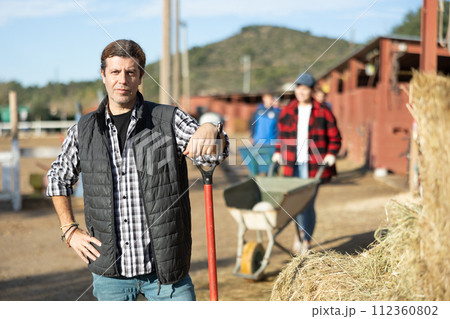 Stable worker collects hay with a pitchfork to feed horses on farm Stable worker collects hay with a pitchfork to feed horses on farm 112360802