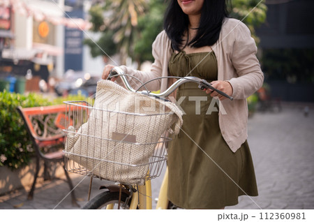 A cropped shot of a woman pushing her bicycle on the street in the city. 112360981