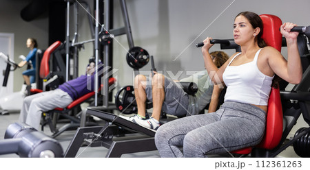 Caucasian woman doing exercises on shoulder press machine in gym Caucasian woman doing exercises on shoulder press machine in gym 112361263