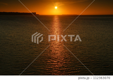 沖縄県国頭郡本部町渡久地 濱元橋からの夕陽と光の道、瀬底島と水納島のシルエット 沖縄県国頭郡本部町渡久地 濱元橋からの夕陽と光の道、瀬底島と水納島のシルエット 112363070