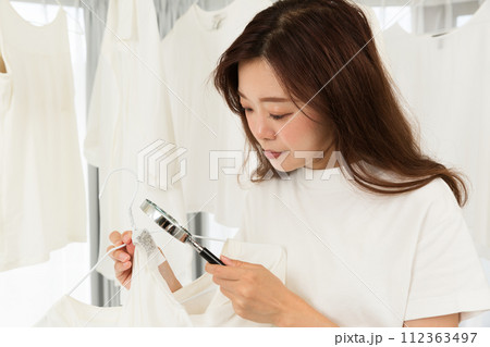 衣服の洗濯表示タグをルーペで拡大する女性. 衣服の洗濯表示タグをルーペで拡大する女性. 112363497