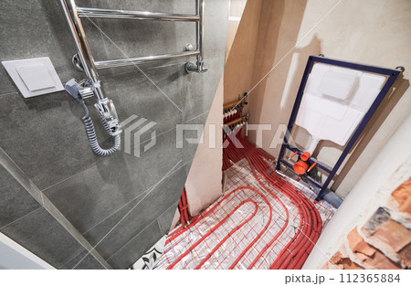 Comparison of washroom lavatory before and after renovation. Old apartment restroom with underfloor heating pipes and new renovated toilet room with electric towel dryer. Comparison of washroom lavatory before and after renovation. Old apartment restroom with underfloor heating pipes and new renovated toilet room with electric towel dryer. 112365884