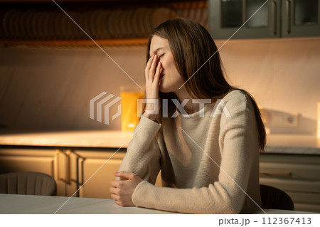 Young Woman Sitting Alone in a Kitchen Showing Signs of Distress 112367413