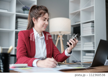 Happy Asian business women have the joy of talking on the smartphone, tablet, and laptop in the home office, Wearing a red suite. 112368536