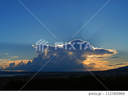 夏の夕方、積乱雲が夕日でオレンジ色に輝き、青空に向かって光が放射状に広がる。印象的で綺麗だ。 112368966