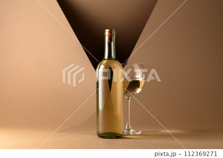 Bottle and glass of white wine on a beige background. 112369271