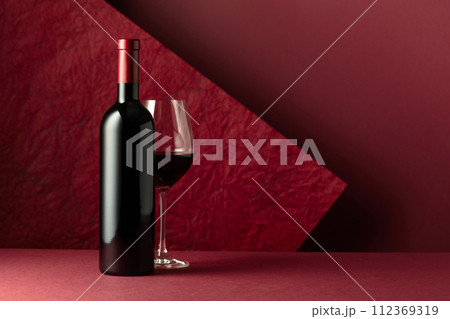 Bottle and glass of red wine on a red background. 112369319