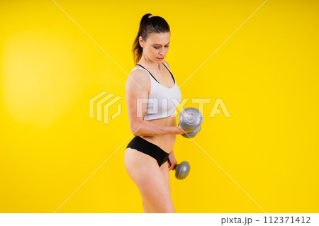 Sporty female doing exercise with dumbbells, silhouette studio shot dark yellow background Sporty female doing exercise with dumbbells, silhouette studio shot dark yellow background 112371412
