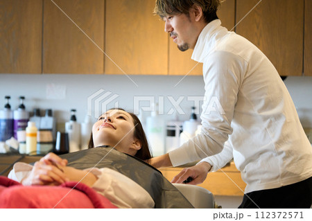 シャンプー台で髪の毛を洗い流す美容師 シャンプー台で髪の毛を洗い流す美容師 112372571