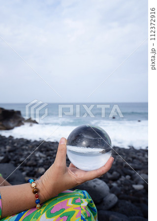 woman meditating on beach shore and holding crystal ball 112372916
